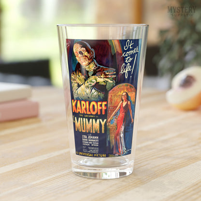 Glass tumbler with a vintage movie poster design featuring 'The Mummy' on a wooden surface. The Mummy 1932 vintage Boris Karloff horror monster movie poster reproduction 16oz clear pint glass home decor glassware from Mystery Supply Co. @mysterysupplyco